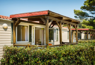 Cabañas Padova Home con porches de madera y setos verdes en Valamar Camping Padova, Croacia, día soleado.