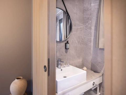 Modern bathroom at Hilltop Green Chalet with marble walls, round mirror and square wash basin.