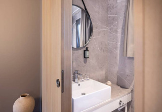 Modern bathroom at Hilltop Green Chalet with marble walls, round mirror and square wash basin.