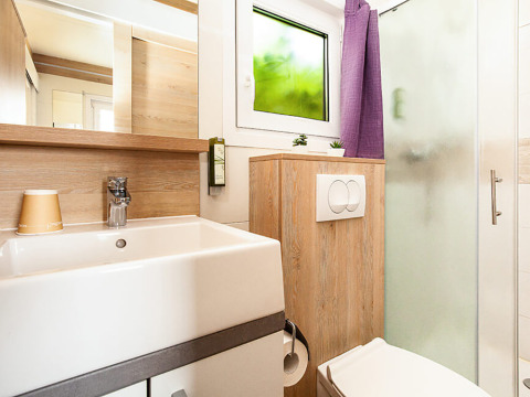 Moderne badkamer met houten details, lavabo, toilet, douche en raam in Sunny Beach Home lodge.