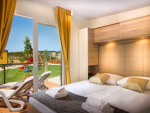 Moderne slaapkamer in Bella Vista Home bij Valamar Camping Krk, Kroatië, met uitzicht op tuin en speeltuin.