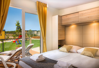 Moderne slaapkamer in Bella Vista Home bij Valamar Camping Krk, Kroatië, met uitzicht op tuin en speeltuin.
