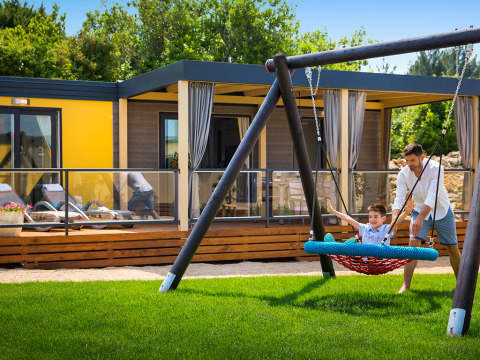 Vader en zoon spelen samen op een schommel bij een Bella Vista Home lodge op Valamar Camping Krk, Kroatië, zonnig weer.