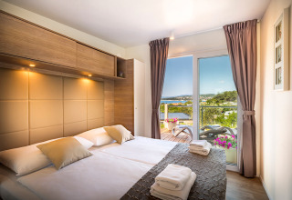 Lichte moderne slaapkamer met tweepersoonsbed, terras- en tuinzicht bij Bella Vista Home Garden terrace, Valamar Camping Krk, Kroatië.