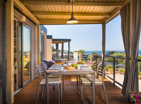 Overdekt terras met tafel, stoelen en uitzicht op zee bij Bella Vista Home, Valamar Camping Krk, Kroatië.