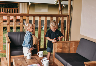Twee kinderen spelen met speelgoed op het terras van een safaritent bij Camping de Kleine Wielen in Nederland.