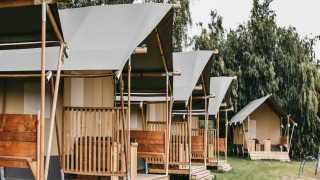 Fila de tiendas safari con baño en camping verde, rodeadas de árboles y cielo nublado al fondo.