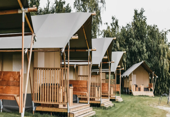 Reihe von Safari-Zelten mit Toilette auf einem grünen Campingplatz mit Bäumen im Hintergrund.