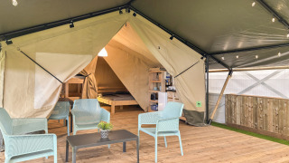 Tente safari avec ouvertures, coin salon moderne sur terrasse en bois, vue sur lit et coin cuisine.