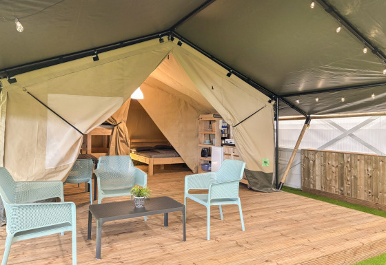 Tienda safari con paneles abiertos, mobiliario moderno en terraza de madera y vista a dormitorio y cocina.
