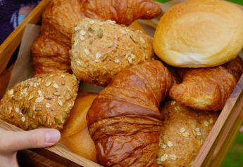 Eine Person hält ein Tablett mit Croissants und Brötchen draußen bei einer Glamping-Unterkunft.