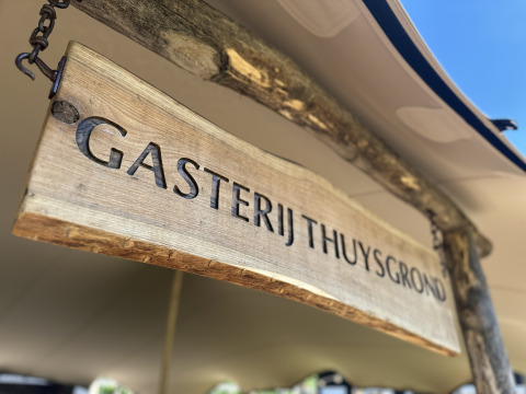 Cartel de madera con el texto 'Gasterij Thuysgrond' en un alojamiento glamping bajo el sol brillante.