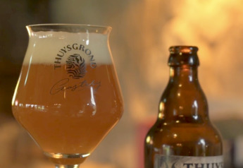 Et glas og en flaske Thuy's Tripel øl står på et bord i hyggeligt, stemningsfuldt glampingmiljø.