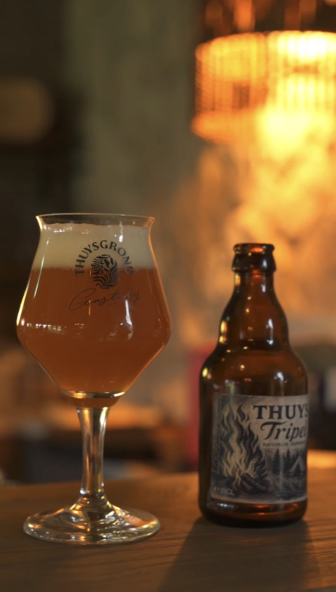 Un bicchiere e una bottiglia di birra Thuy's Tripel su un tavolo in un'accogliente struttura di glamping.