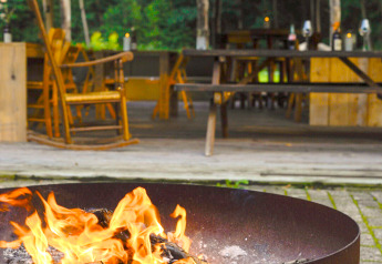 Braciere acceso all'aperto davanti a una sistemazione glamping con arredi rustici in legno e atmosfera accogliente.