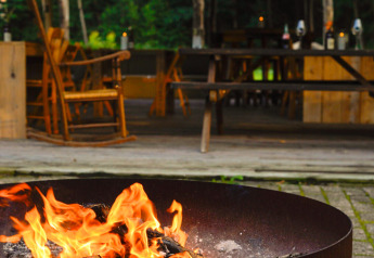 Feuerschale im Freien vor einem stilvollen Glamping-Bereich mit rustikalen Holzmöbeln und Naturblick.