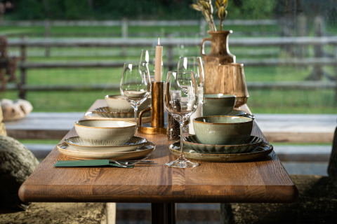 Tavola apparecchiata all’aperto in un glamping con piatti di ceramica e bicchieri, vista sulla natura.