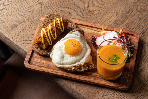 Petit déjeuner en glamping avec œuf au plat sur pain, croquette à la moutarde, salade et jus de fruit.