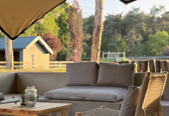 Zona lounge all'aperto in glamping con mobili in legno, cuscini comodi e vista sulla natura.