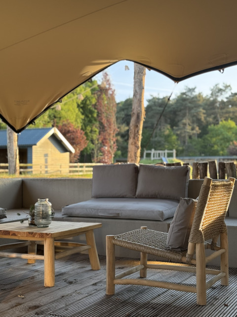 Glamping zithoek buiten met houten meubels, zachte kussens en een prachtig uitzicht op de natuur.