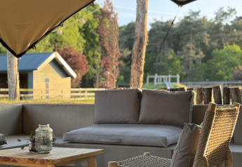 Zona de descanso exterior en glamping con muebles de madera, cómodos cojines y vista natural.