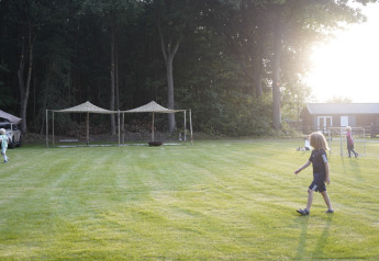 Kinder spielen auf einer Wiese bei Glamping-Unterkunft, Zelte und Wald im Sonnenuntergang.
