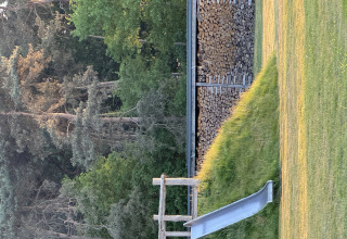 Rutsche auf einer Wiese neben einem Holzstapel an einem Waldrand auf einer Glamping-Unterkunft.
