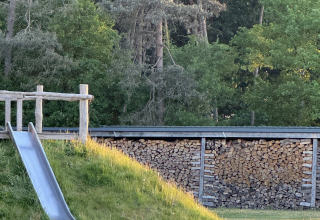 Scivolo metallico su prato accanto a una legnaia in un'area boschiva presso una sistemazione glamping.