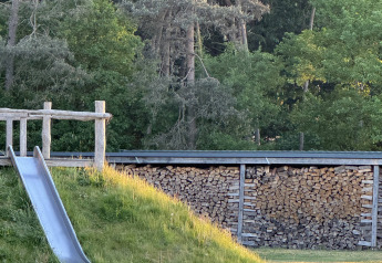 Rutsche auf einer Wiese neben einem Holzstapel an einem Waldrand auf einer Glamping-Unterkunft.