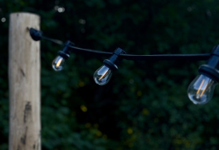 Guirnalda de luces exteriores en un poste de madera junto a una carpa Bell, rodeada de verde al atardecer.