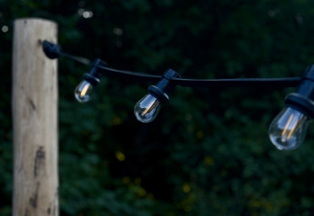 Lichterkette im Freien an einem Holzpfosten bei einem Bell-Zelt, umgeben von grüner Natur in der Dämmerung.