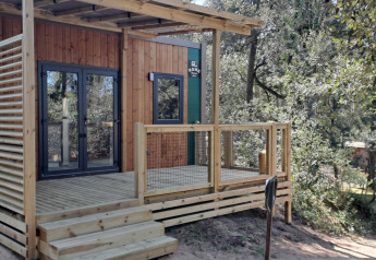 Cabaña Homeflower Premium de 18m² con terraza de madera, situada entre árboles en un entorno natural.