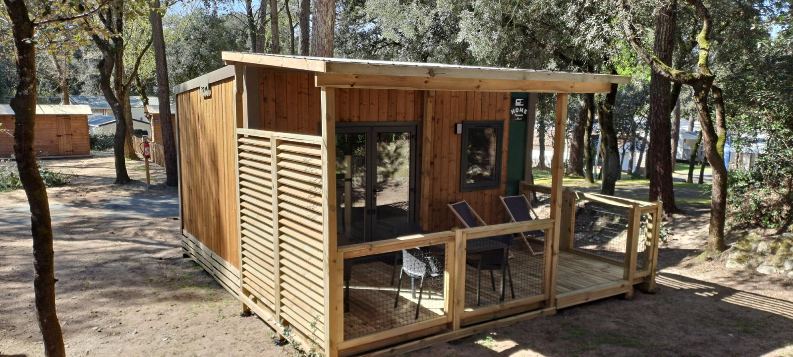 Homeflower Premium 18m² houten lodge met overdekt terras bij Flower Camping La Sagne, omgeven door bomen in Frankrijk.