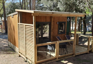 Homeflower Premium 18m² houten lodge met overdekt terras bij Flower Camping La Sagne, omgeven door bomen in Frankrijk.