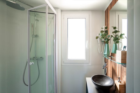 Salle de bain moderne avec douche, fenêtre, vasque et plantes vertes au SunLodge Mobile Home Catalpa, Italie.