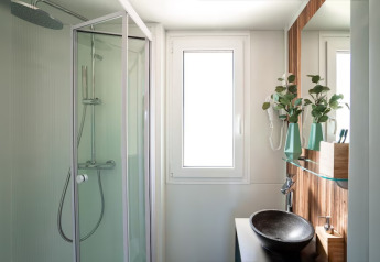 Modern bathroom with a shower, window, vessel sink, and green plants at SunLodge Mobile Home Catalpa, Italy.