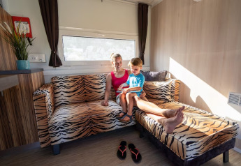 Madre e hijo sentados juntos en un sofá de estampado tigre en SunLodge Mobile Home, Marina di Venezia, Italia.