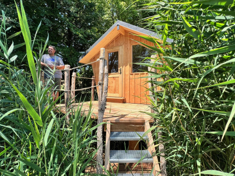 Man op het terras van een houten tiny house, verscholen tussen rietplanten bij Domaine des Feuilles, Frankrijk.