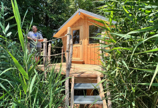 Man op het terras van een houten tiny house, verscholen tussen rietplanten bij Domaine des Feuilles, Frankrijk.