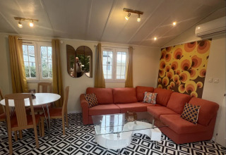 Hyggelig stue i Premium Mobile Home på Campsite Les Franquettes, med orange sofa og retro tapet.