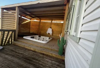 Udendørs terrasse med overdækket jacuzzi, håndklæde, kaktusdekoration og trægulv ved mobilhome.