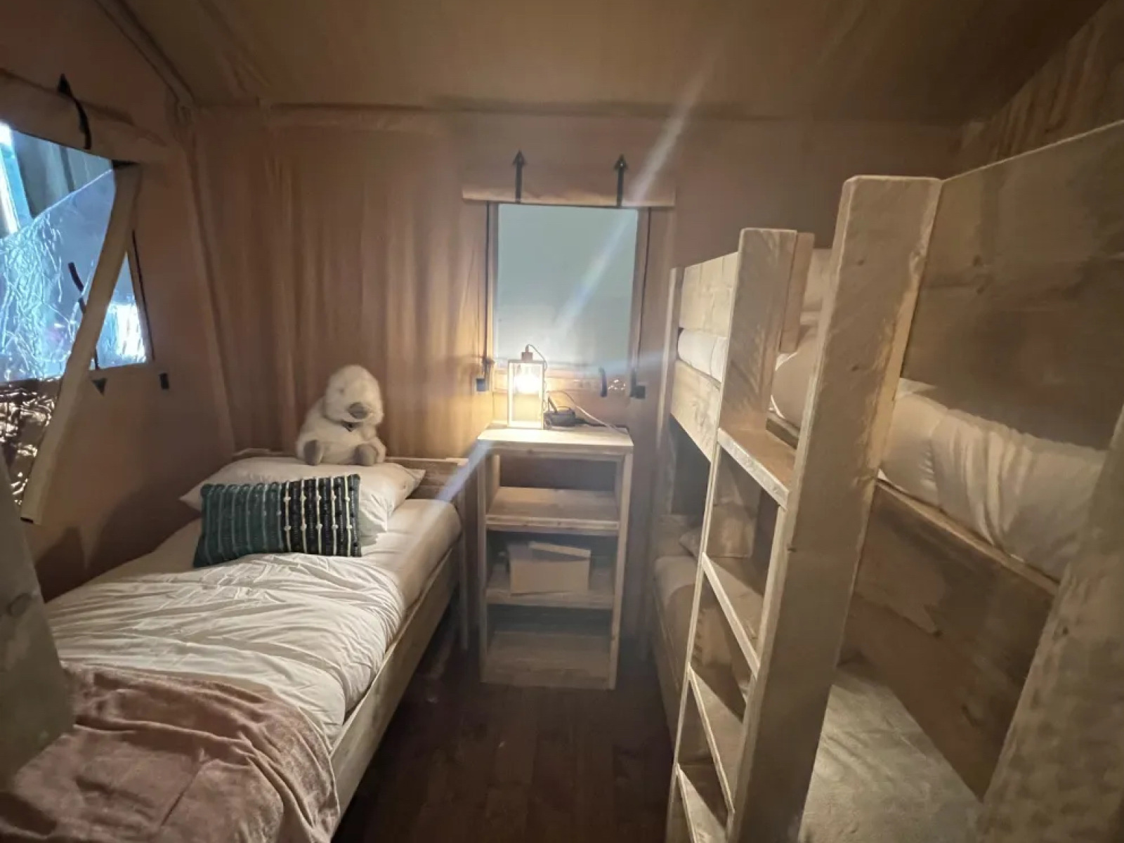 Interieur van Lodge Woody 38 met stapelbedden, eenpersoonsbed en warme verlichting op Camping Les Franquettes.