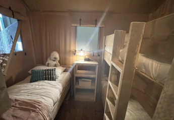 Innenaufnahme von Lodge Woody 38 mit Etagenbetten, Einzelbett und gemütlicher Beleuchtung auf Camping Les Franquettes.
