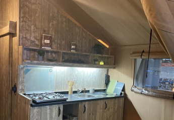 Vista interna della tenda safari Lodge «Woody 38» con cucina rustica al campeggio Les Franquettes.