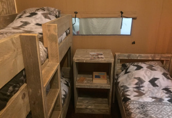 Interior de la tienda safari Luxury Lodge 40 en el camping Les Franquettes en Francia, con literas y cama individual.
