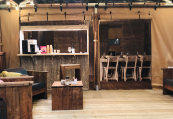 Interno di tenda safari di lusso con salotto e tavolo in legno al campeggio Les Franquettes in Francia.