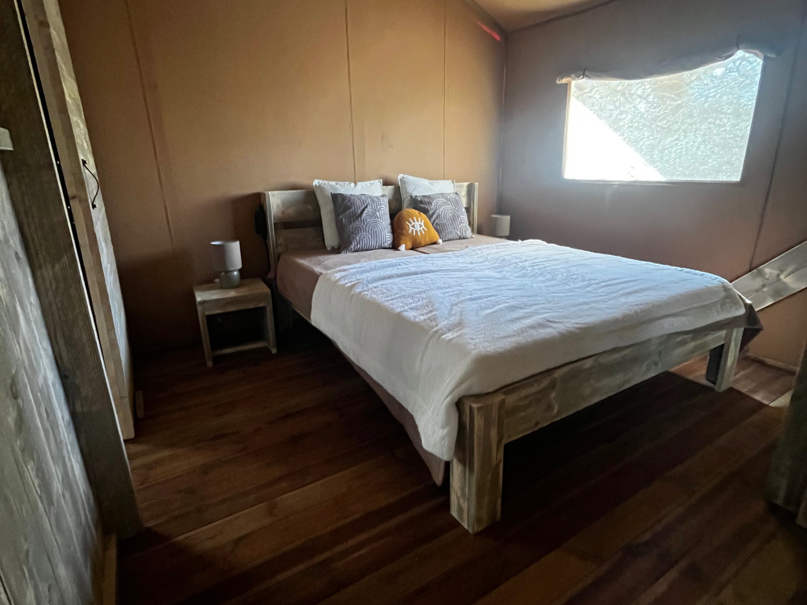 Slaapkamer in luxe safaritent bij camping Les Franquettes in Frankrijk, met houten bed en meubels.