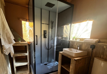 Baño de una tienda safari de lujo con ducha moderna, lavabo y váter en el camping Les Franquettes en Francia.