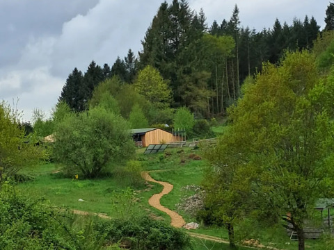 Scenic view of grassy area, trees, winding path and wooden cabin at Campsite Junora, France under cloudy skies.