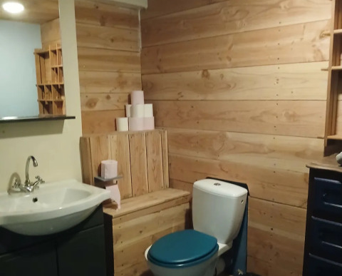 Landelijke badkamer met houten bekleding, blauw toiletdeksel en wc-papier in Emperor Bell Tent, Junora, Frankrijk.